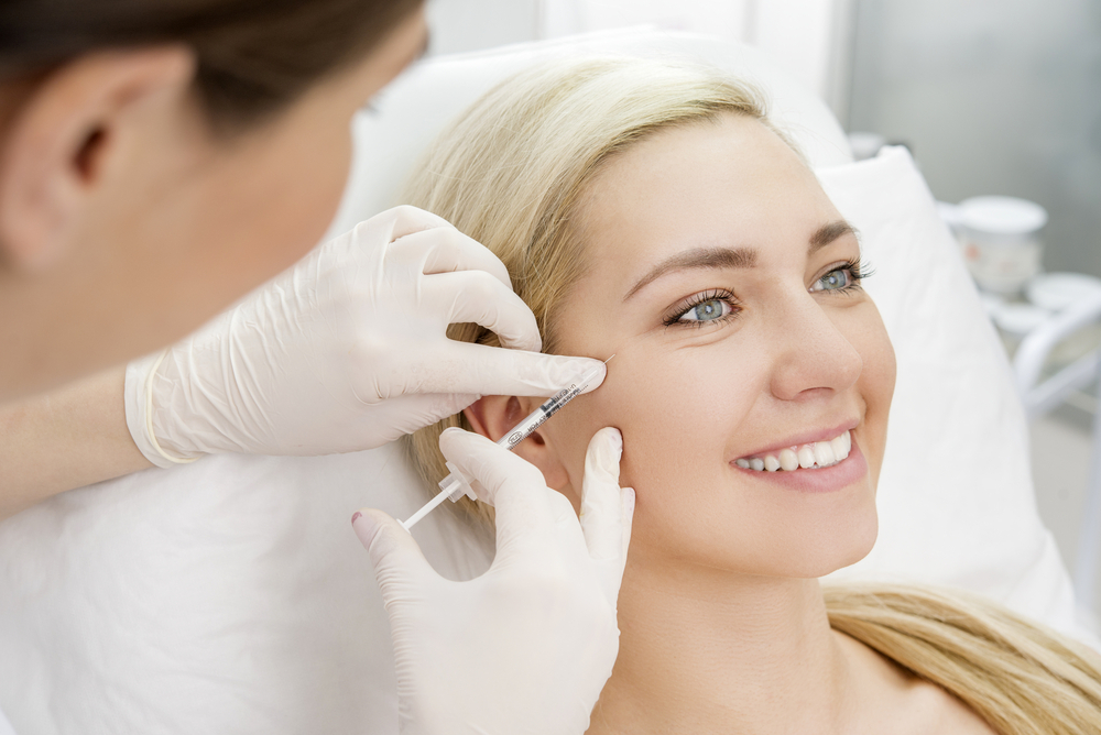 Aesthetic treatment session showing a healthcare professional administering an injectable procedure to a smiling female patient in a clinical setting.